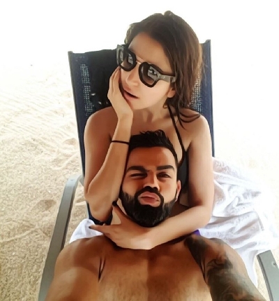 Virat Kohli posted a selfie on Instagram where he can be seen lying with his head on wife Anushkaâ€™s lap, who is sitting on a lounge chair on a sandy beach. In the selfie, which has the appearance of a watercolour painting due to a filter, Anushka flaunts a black bikini and shades. The actress seems to be staring at something while hubby Virat winks an eye looking at the camera and pouts for the selfie.